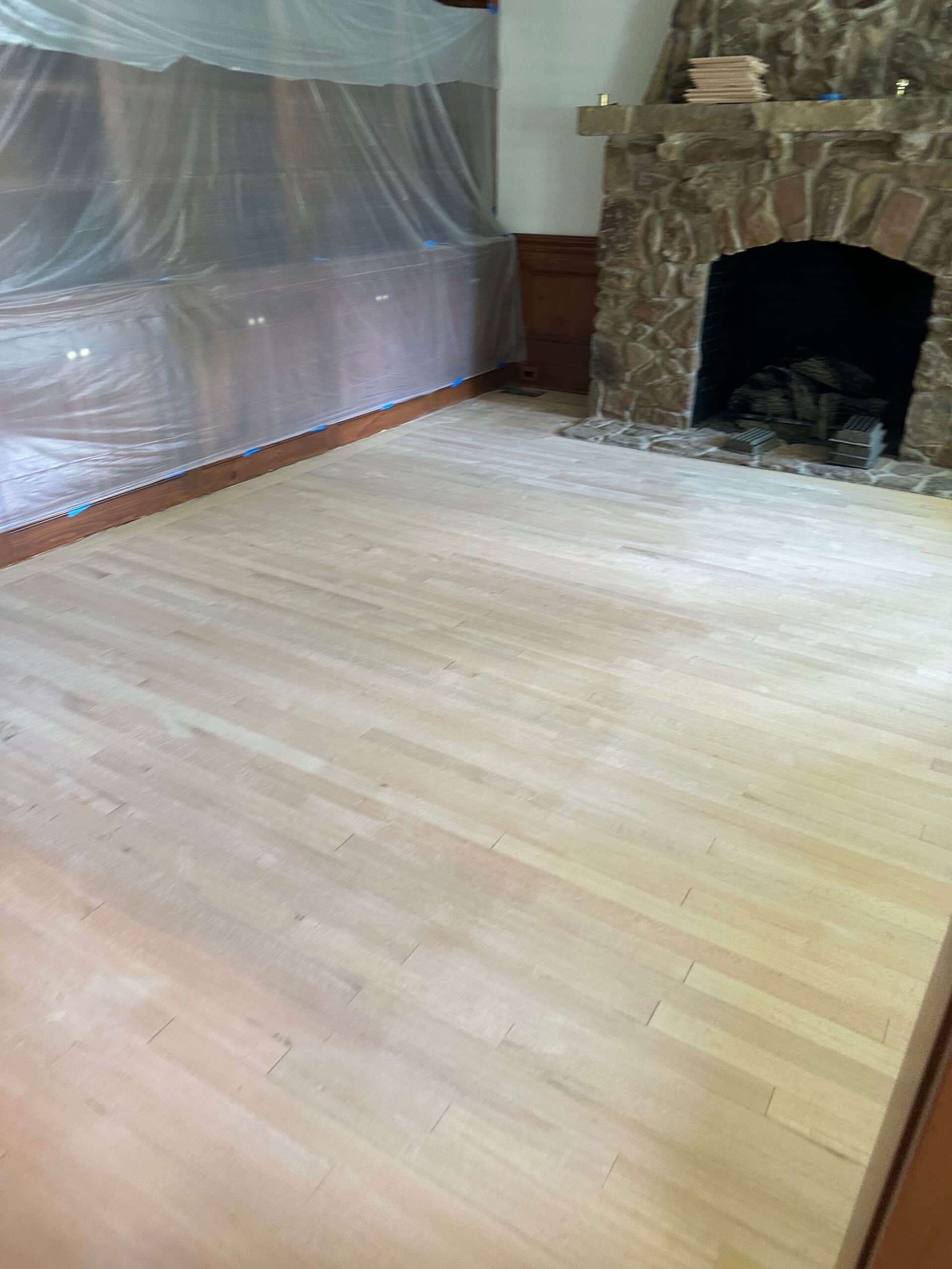 Raw hardwood floor sanded smooth and ready for stain in a room with a stone fireplace